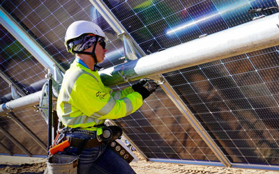 worker wearing helmet and high visibility jacket uses tools on a solar panel